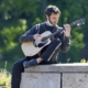 Strumming guitar in nature on stone bench